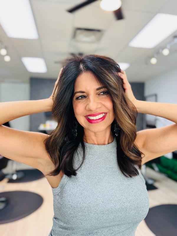 Smiling woman with wavy hair poses confidently in a bright room.