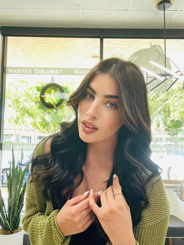 Woman with long dark hair and green sweater posing indoors.