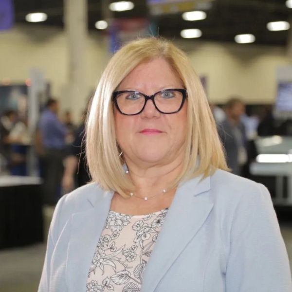 Professional woman with blonde hair and glasses in a conference setting.