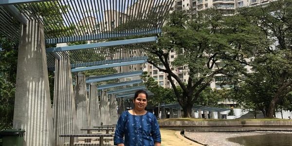 Woman standing in a park with modern pergola and trees.