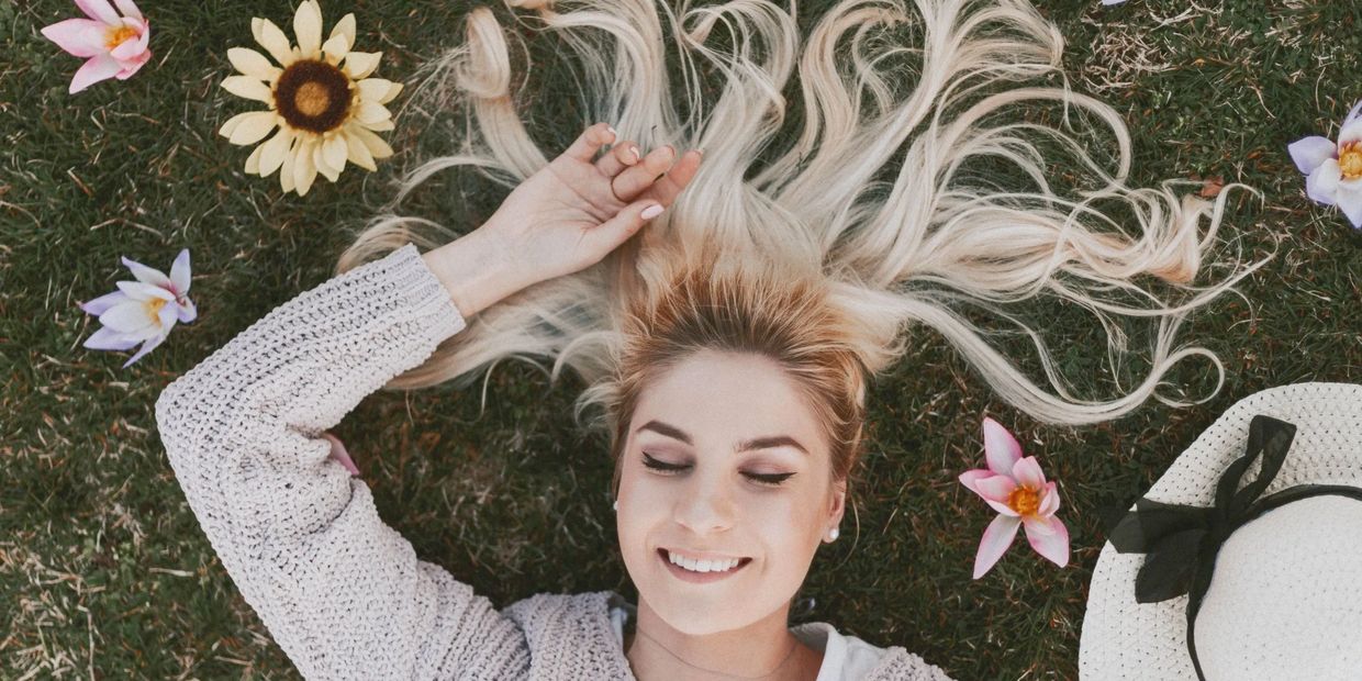 girl laying on lawn with colorful flowers around her flowing long blonde hair 