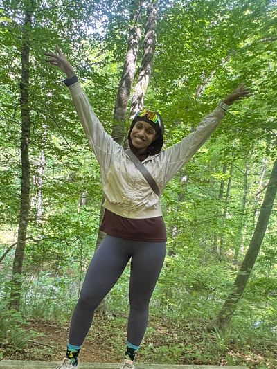 Woman enjoying a sunny day in the forest with arms raised.