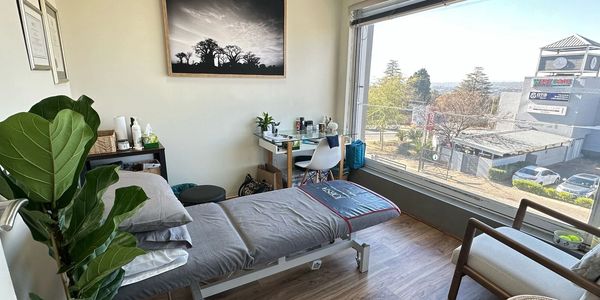 A cozy and bright therapy or massage room with a large window and wooden floor.