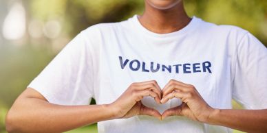 Person making heart shape with hands, wearing volunteer shirt.