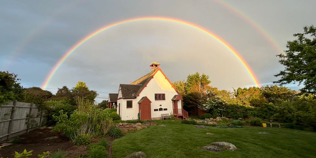 A charming house with a vibrant double rainbow overhead in a lush garden.