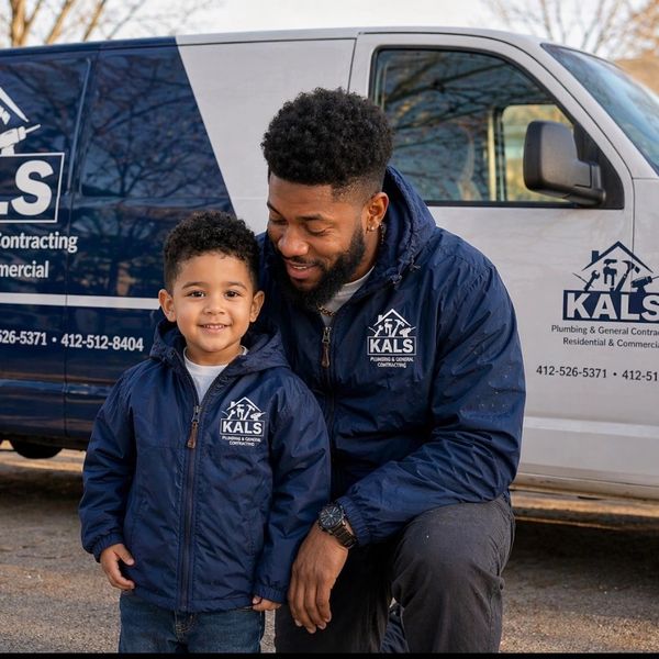 Father and son in matching jackets by a KALS plumbing van.