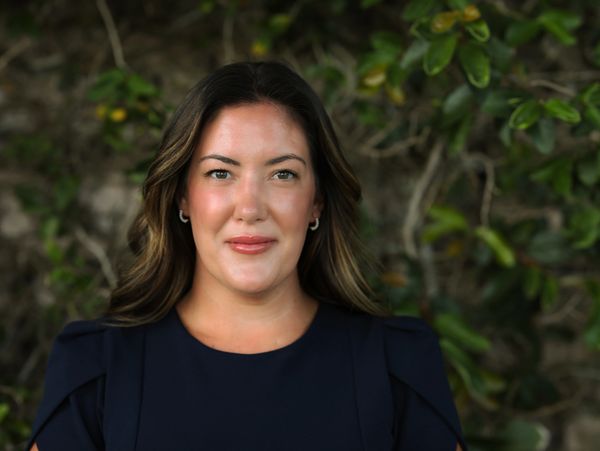 Woman with dark hair in navy blue top smiling outdoors.
