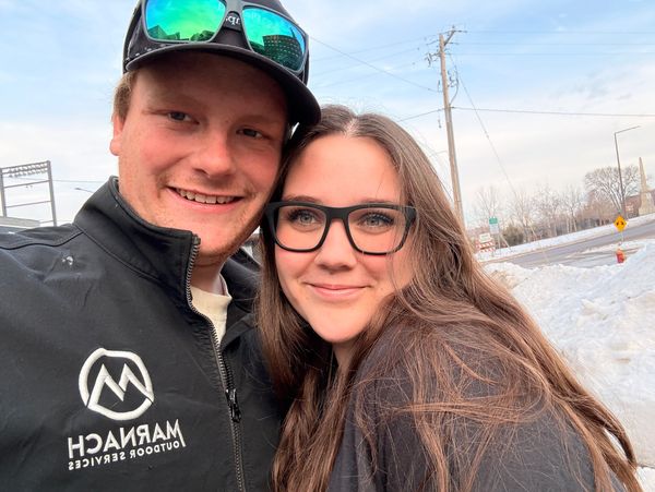 A smiling couple outdoors in winter clothing with snow in the background.