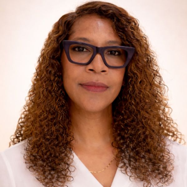 Woman with curly hair and black glasses wearing a white top.
