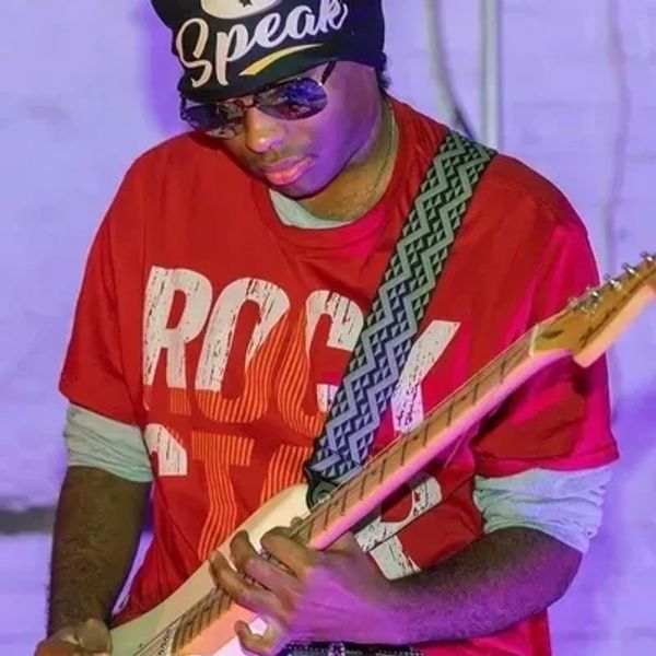 Man in red shirt playing electric guitar with a patterned strap.
