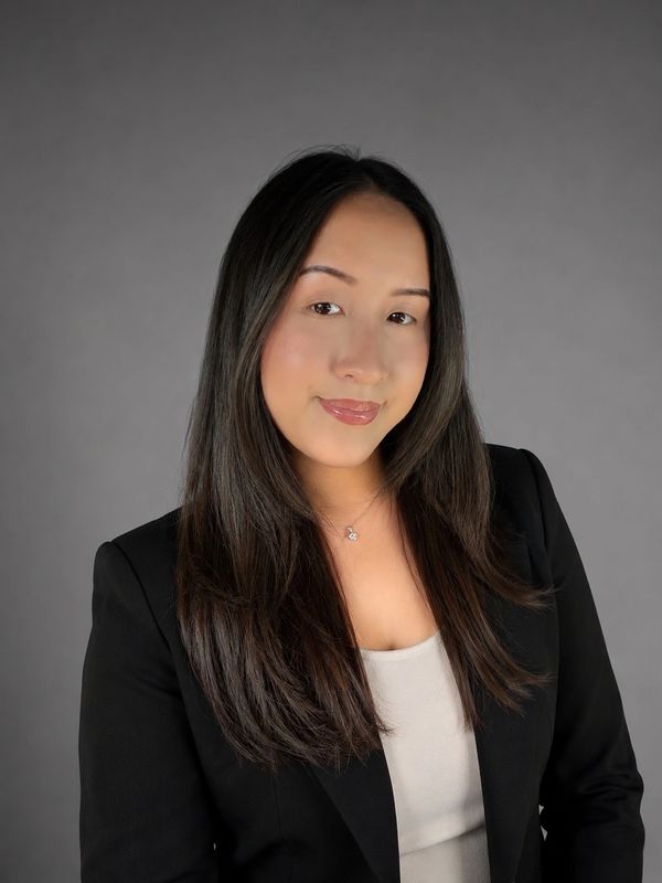 Confident woman with long hair, wearing a black blazer and beige top.
