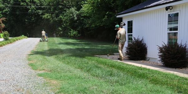 Two men maintaining a lawn near a white building.
