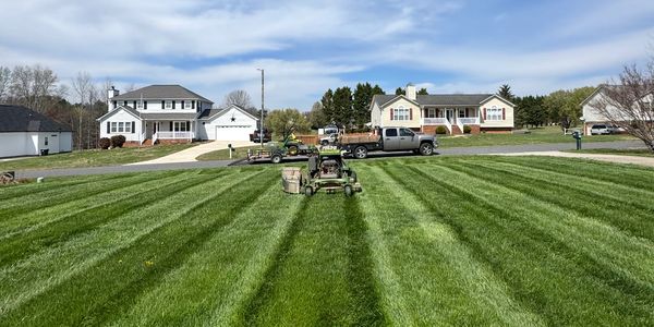 A lawnmower creating striped mowing patterns on a large green lawn.