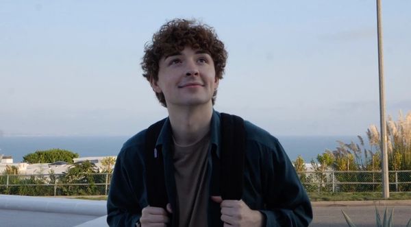 Young man with curly hair looking up and smiling outdoors near the coast.
