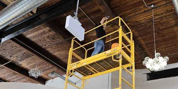 Person working on ceiling lighting while standing on a tall yellow scaffold in a bridal store.