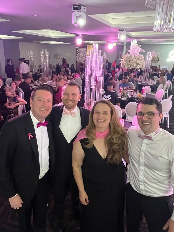 Four people dressed formally at an event with pink accents.
