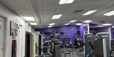 Modern gym interior with various workout machines and purple accent walls.