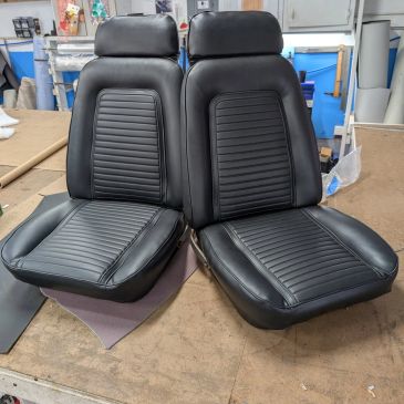 Two black leather car seats placed on a workshop table.