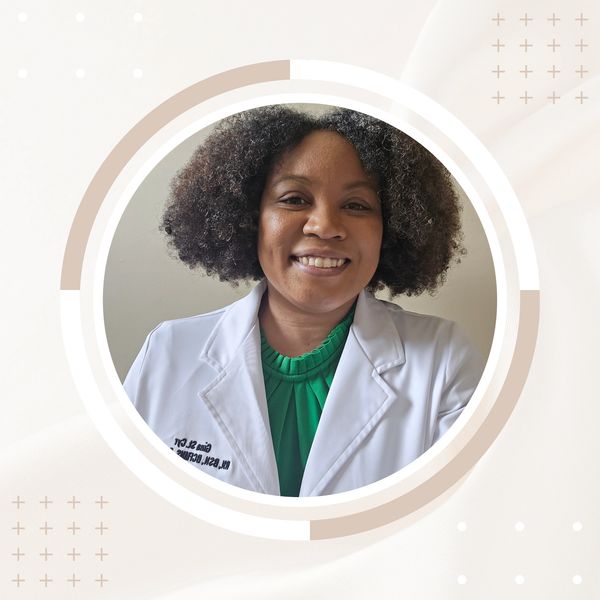 Smiling woman in a white medical coat and green blouse.