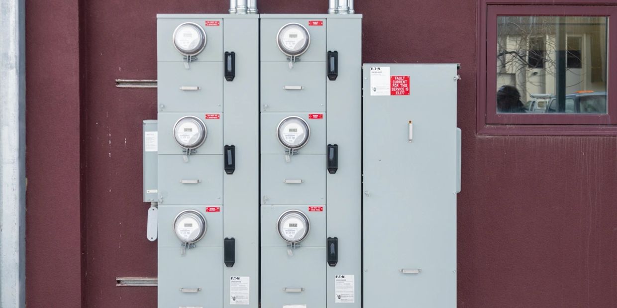 A set of gray electrical meters mounted on a wall next to a window.