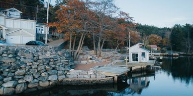 Rock seawall in front of a tan house. rock wall has a small house on it and docks. 