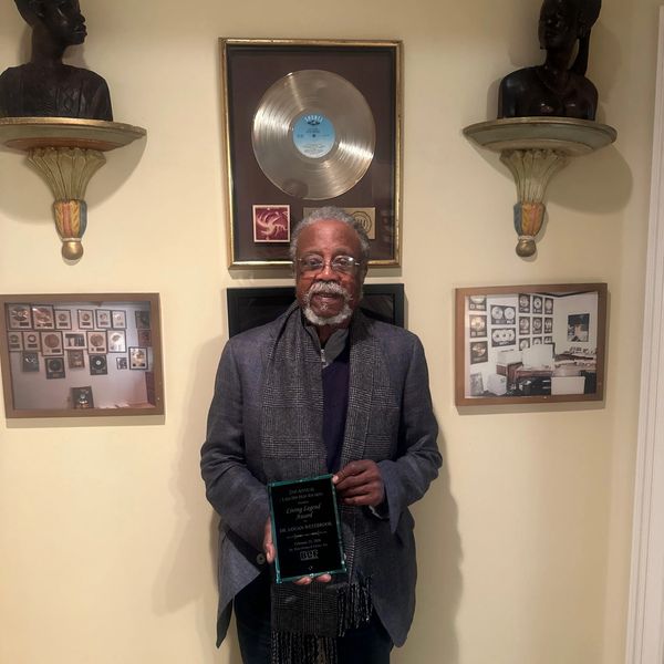 Man holding a plaque in front of framed awards and sculptures.