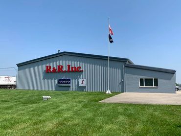 R&R, Inc. building with flags and green lawn under clear blue sky.