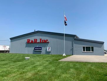 R&R, Inc. building with flags and green lawn under clear blue sky.