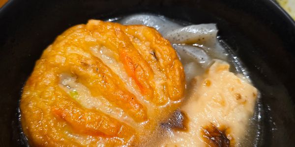 Close-up of fried fish cakes in broth in a black bowl.