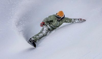 Snowboarder carving deeply through fresh powder snow on a steep slope.