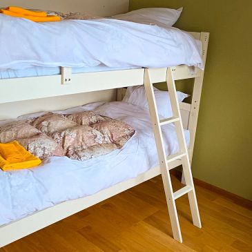 White bunk bed with neatly made beds and yellow towels on wooden floor.