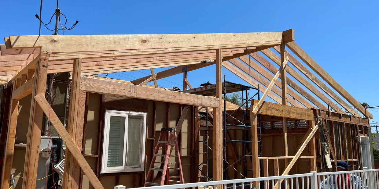 Wooden frame of a house under construction against a clear blue sky.