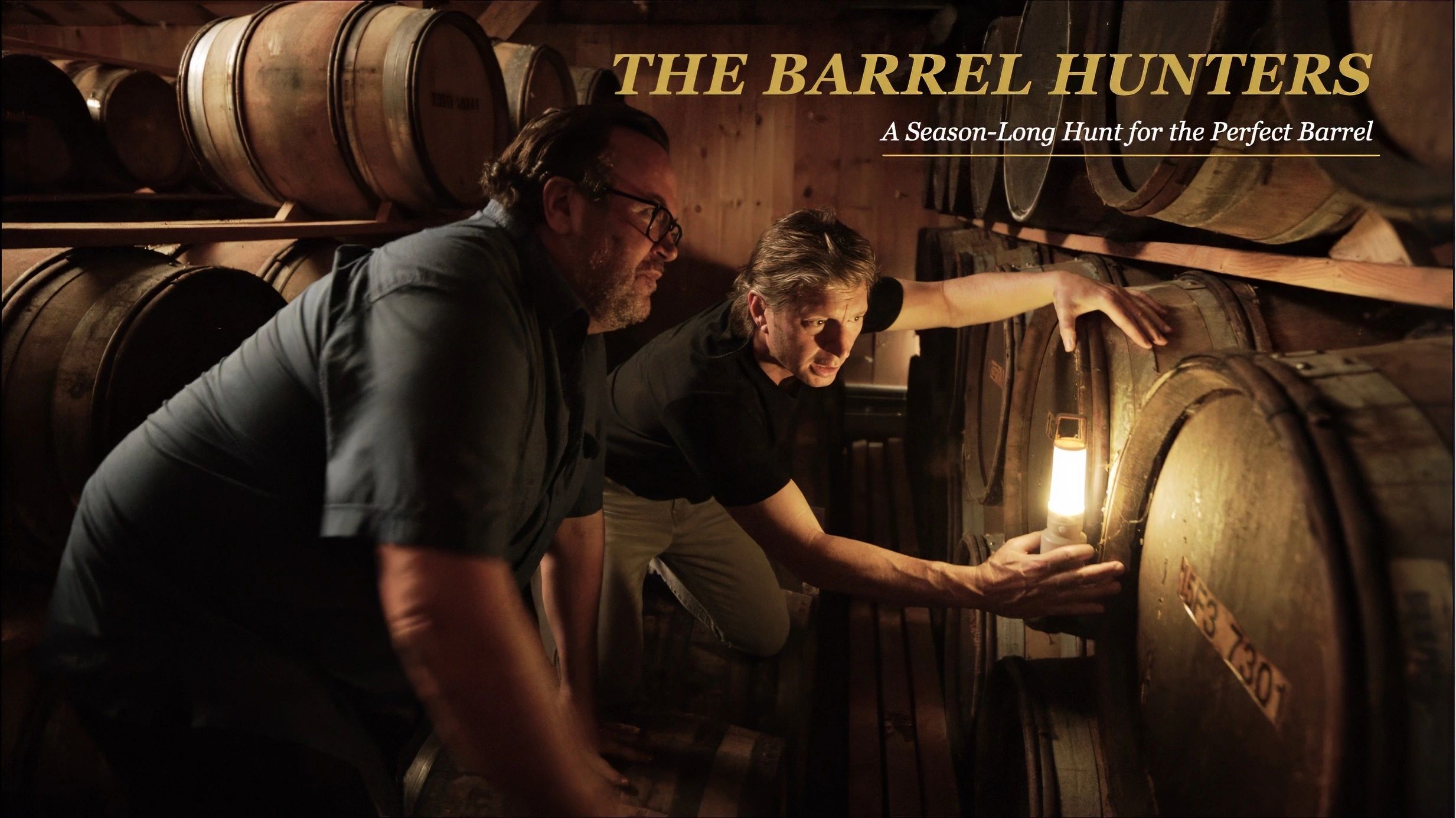 Two men inspect barrels in a dimly lit cellar titled 'The Barrel Hunters.'