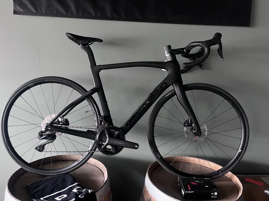 Matte black Pinarello road bike displayed indoors on wooden barrels.