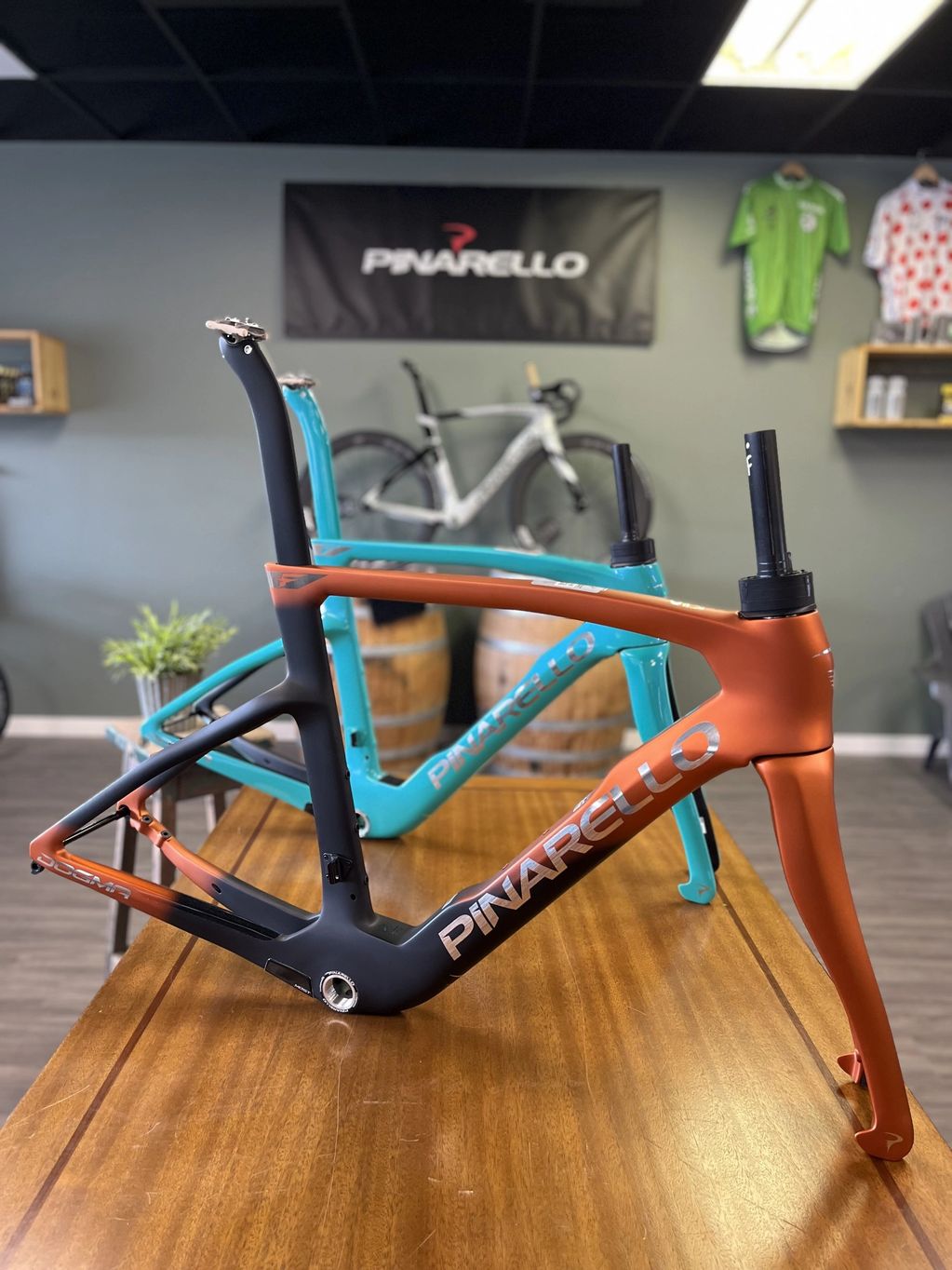 Two Pinarello bicycle frames, one black-orange and one turquoise, displayed on a wooden table.