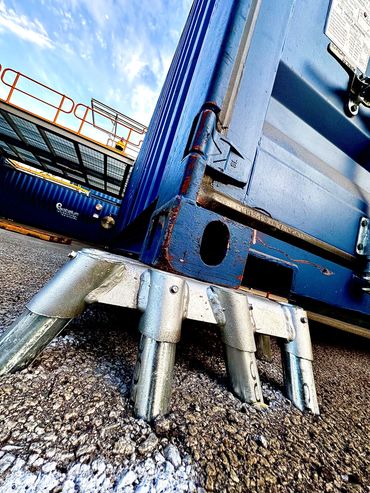 a shipping container sitting on a metal footing that is mounted into bitumen
