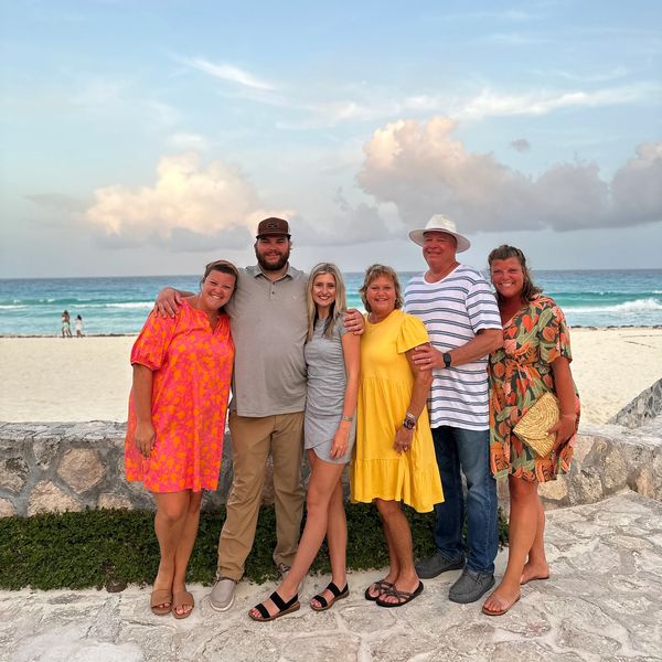 A group of five adults, three women and two men, are standing together on a paved area