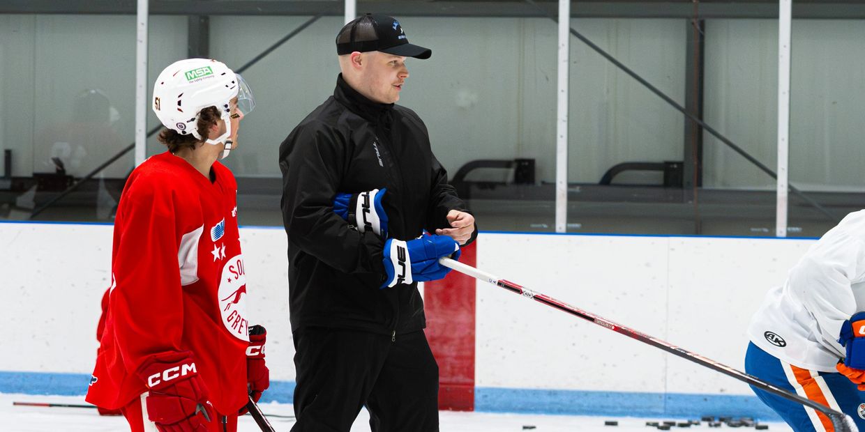 Hockey coach instructing player on ice rink.
