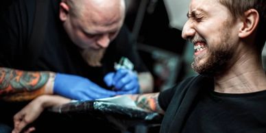 Man getting a tattoo on his arm with a pained expression