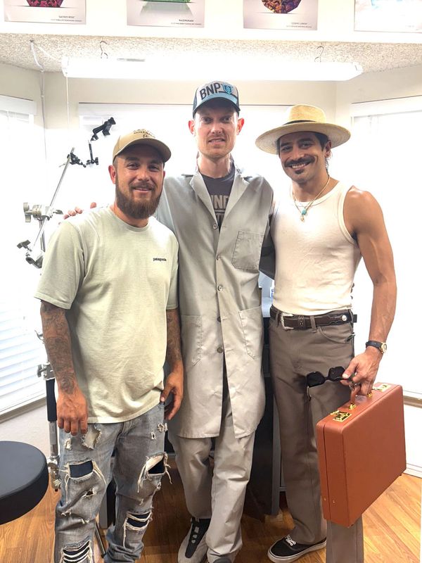 Three men posing indoors with gemstone posters above them.