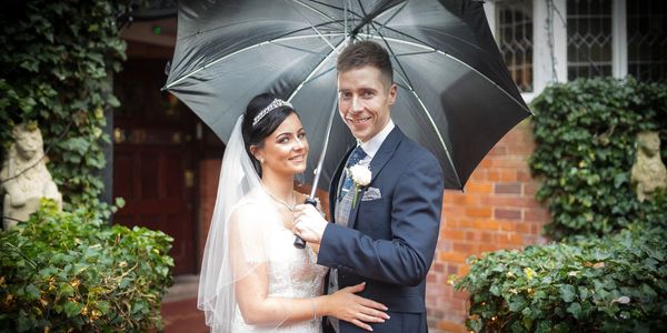 Newlywed couple smiling under an umbrella on their wedding day.