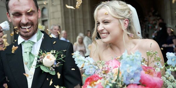 Joyful bride and groom laughing as confetti flies around them after their wedding.
