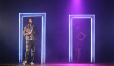 Two people standing in illuminated door frames on a stage with purple lighting.