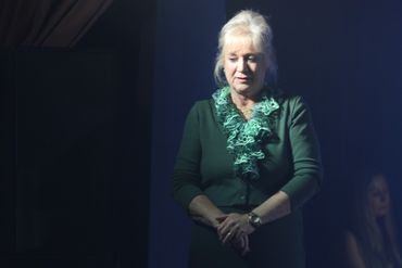 A woman in a green dress stands in dramatic lighting on stage.