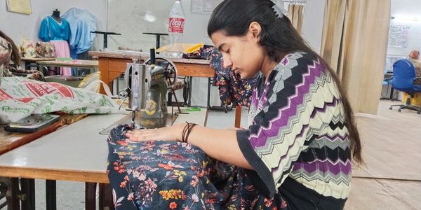 A woman sewing fabric using a sewing machine in a tailoring workshop.