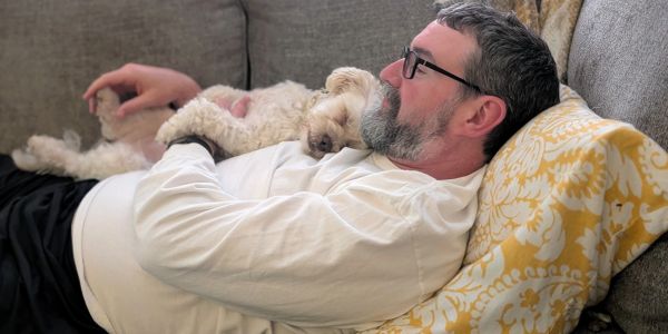 Man lying on sofa cuddling a small dog.
