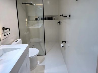 Minimalist white bathroom with black fixtures and a glass shower partition.