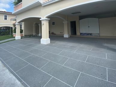 Spacious driveway with tiled flooring and arches at the entrance of a beige-colored house.