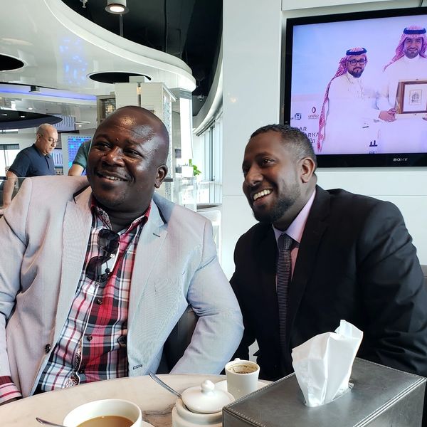 Two men in suits smiling and chatting over coffee in a modern cafe.