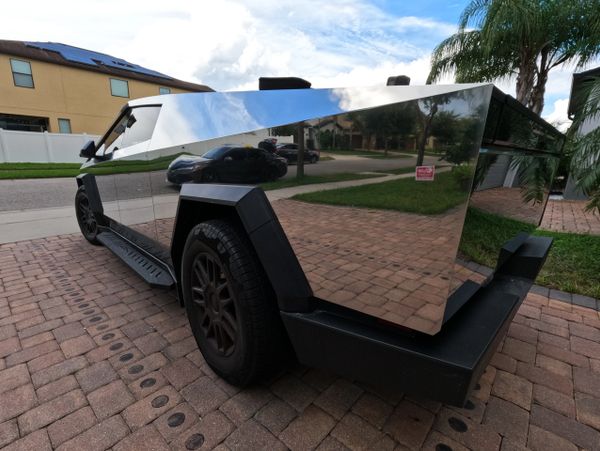 Futuristic Tesla Cybertruck with a reflective stainless steel body parked on a driveway.